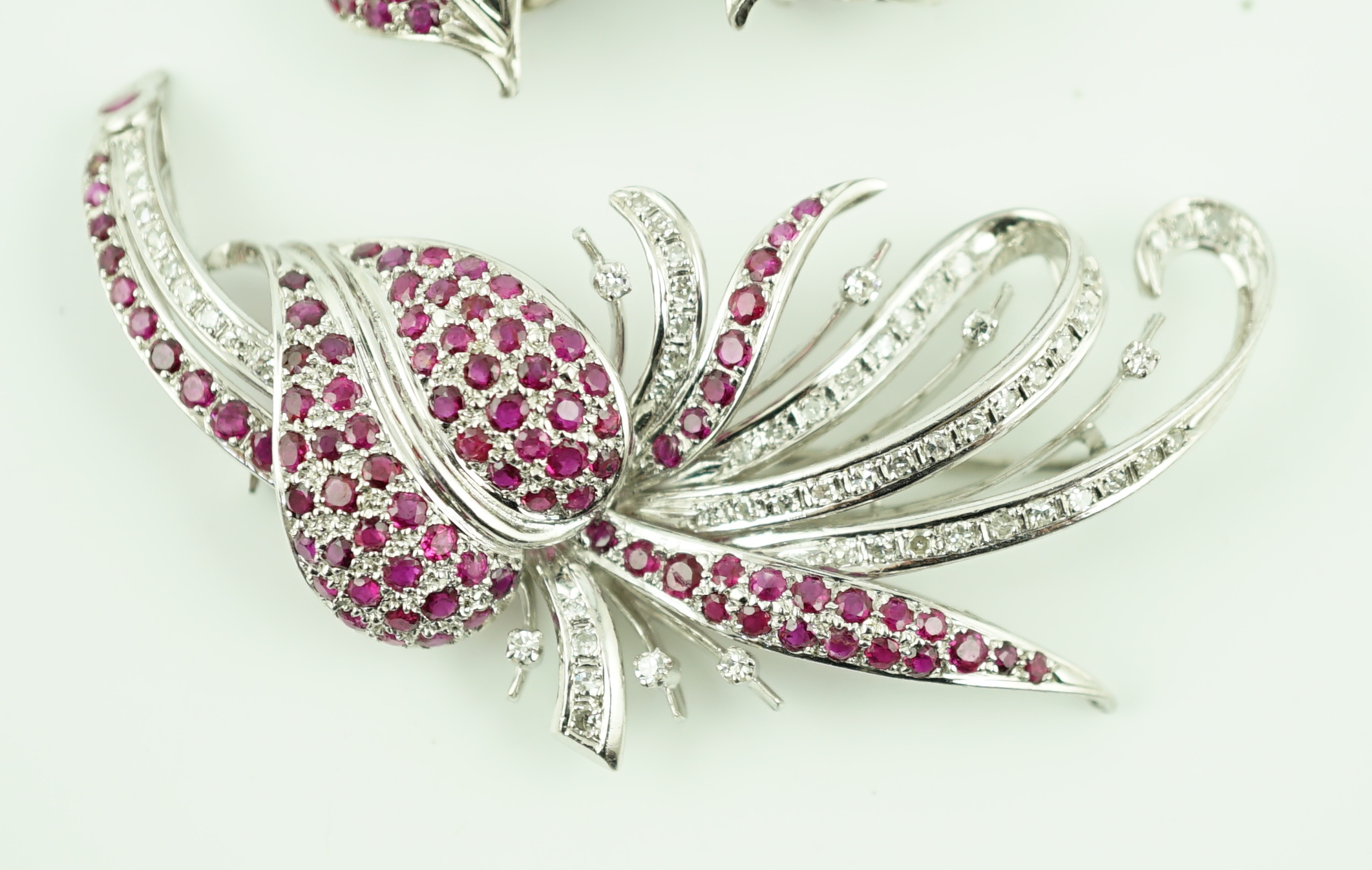 A suite of platinum?, diamond and ruby set cluster jewellery, comprising a spray brooch and pair of matching ear clips